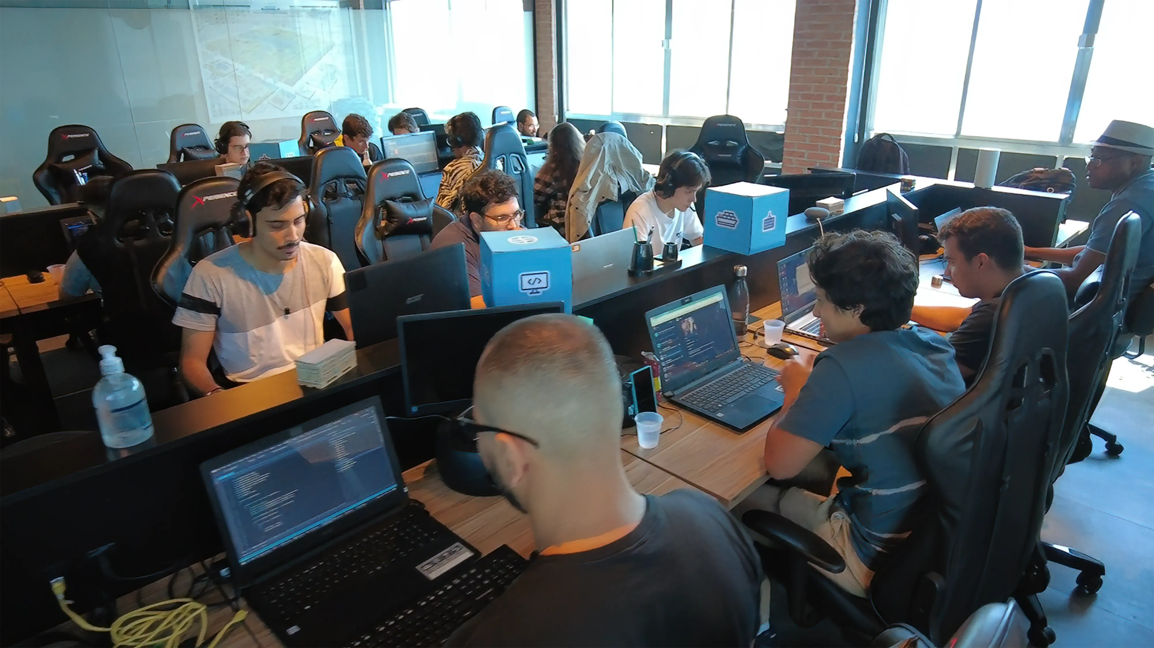 Close em monitor exibindo código-fonte em editor dark mode, com caixas da marca Docker sobre a mesa de desenvolvimento.